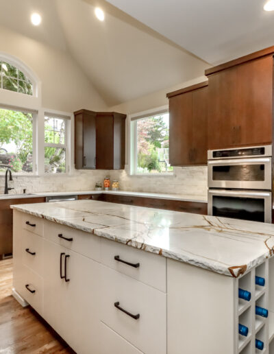 Modern kitchen with dark wood cabinets, a marble island, stainless steel appliances, and large windows providing natural light.
